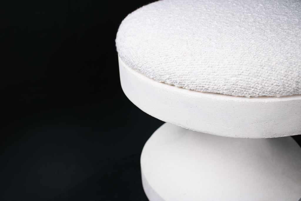 The Tambour barstool in white. The sculptural pedestal base features three stacked hourglass tiers that widen and narrow in alternating rhythm, topped with a round white bouclé upholstered seat.