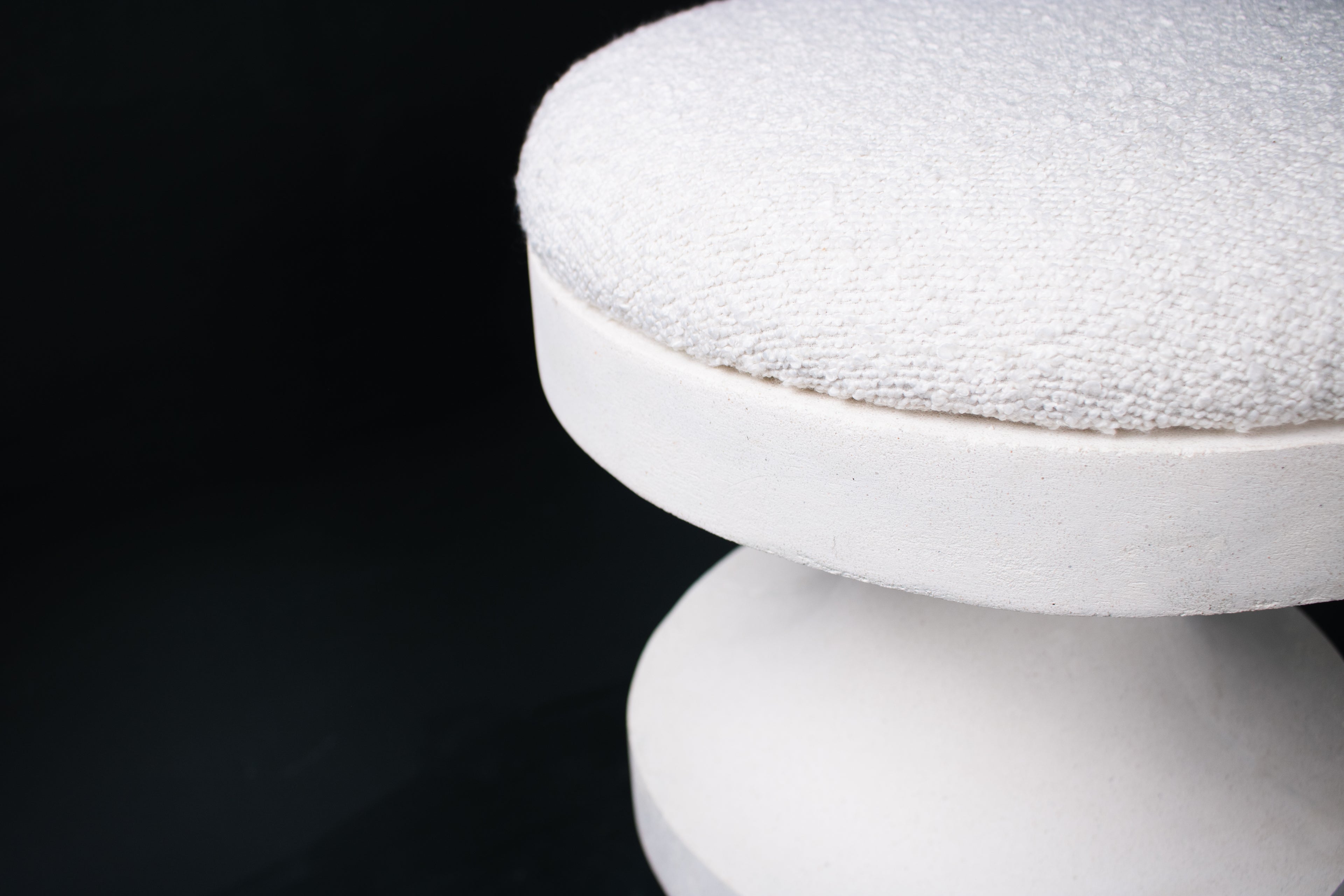The Tambour barstool in white. The sculptural pedestal base features three stacked hourglass tiers that widen and narrow in alternating rhythm, topped with a round white bouclé upholstered seat.