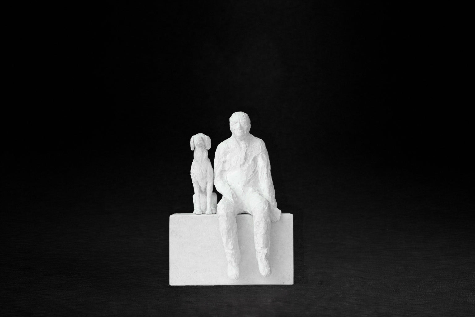 White plaster sculpture of a man sitting on a stone plinth beside his dog, both gazing outward.