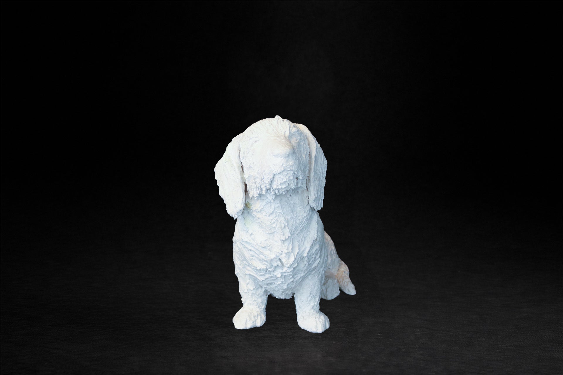 White plaster sculpture of a seated dachshund with an expressive upward gaze.