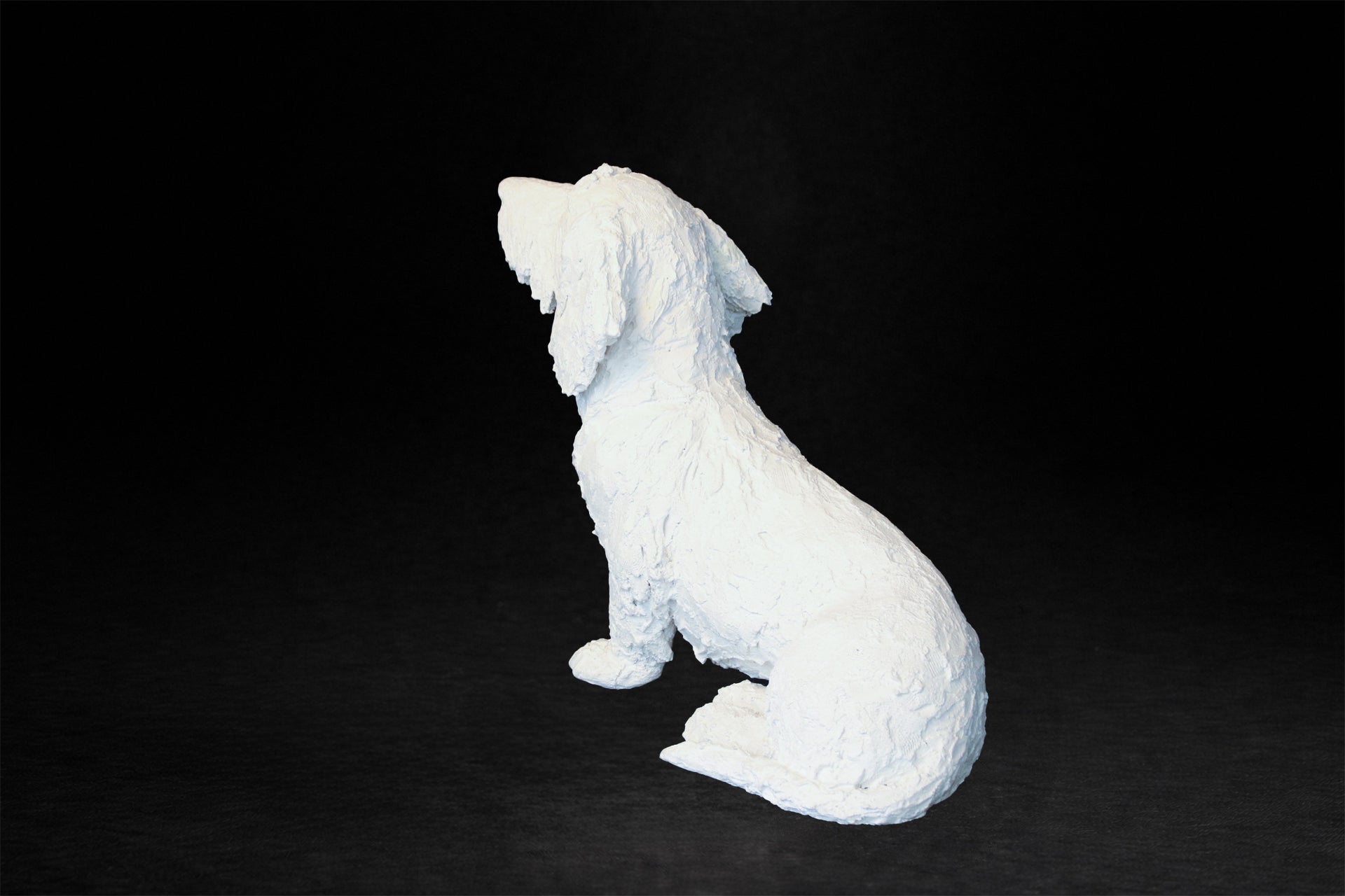 White plaster sculpture of a seated dachshund with an expressive upward gaze.