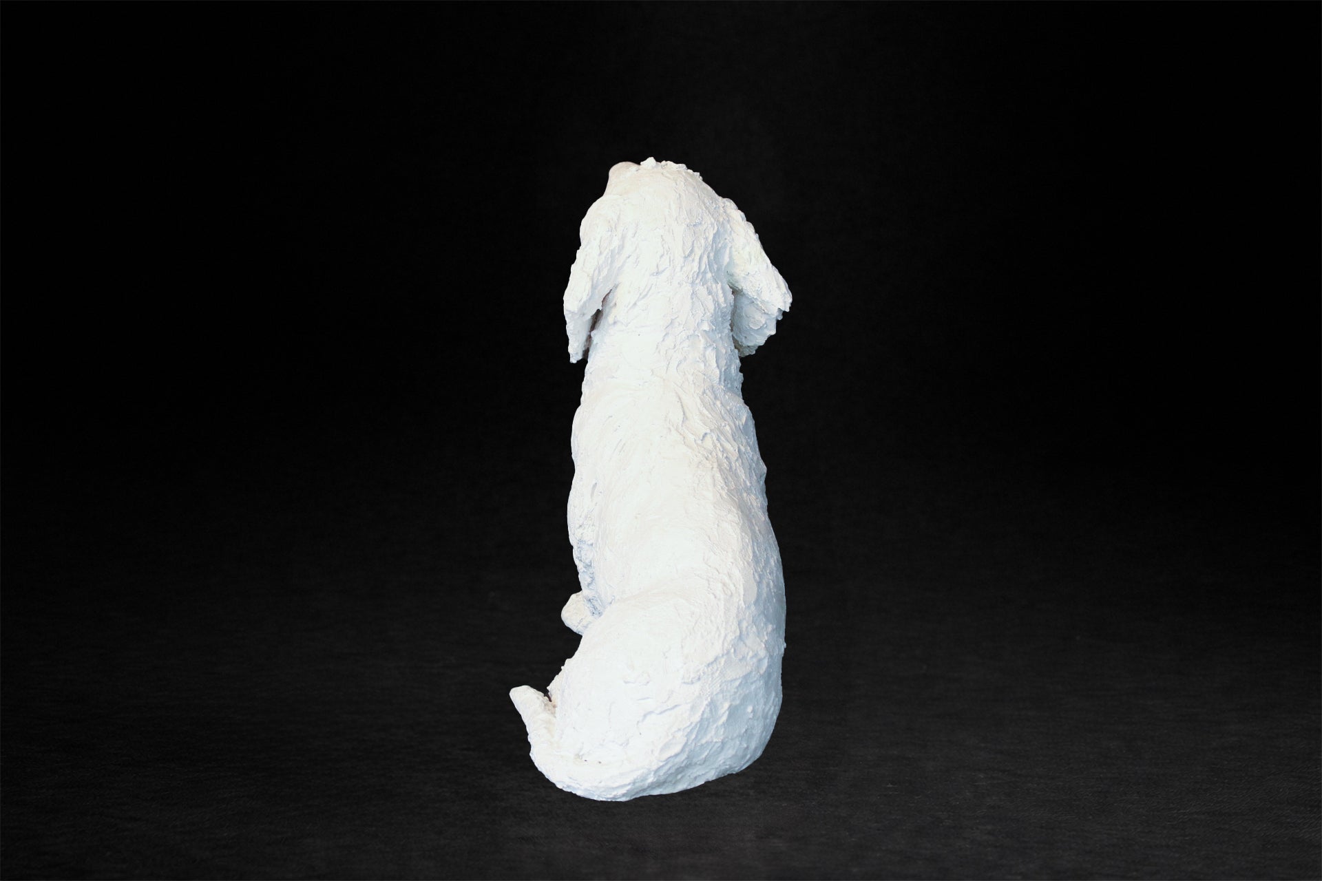 White plaster sculpture of a seated dachshund with an expressive upward gaze.