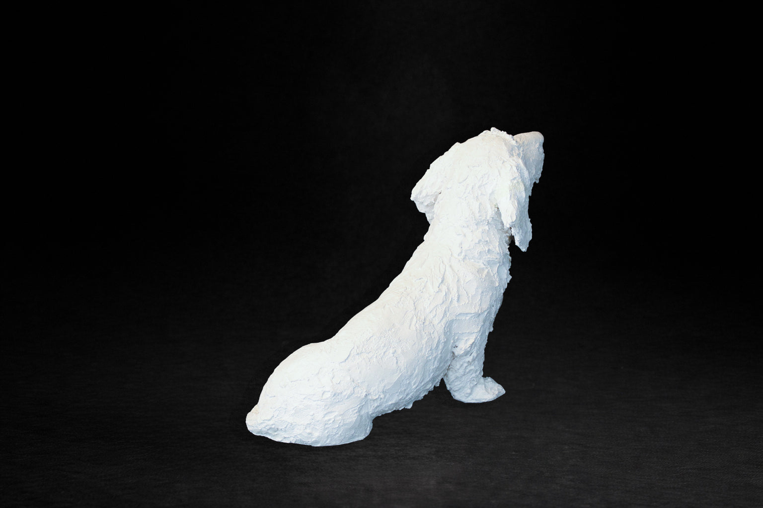White plaster sculpture of a seated dachshund with an expressive upward gaze.