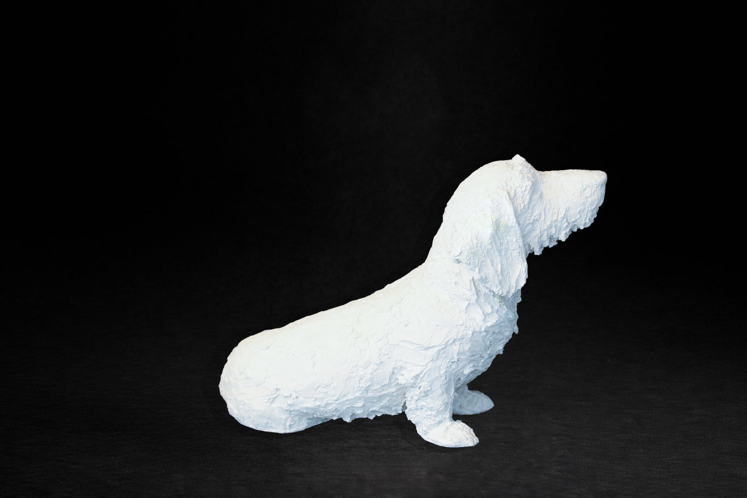 White plaster sculpture of a seated dachshund with an expressive upward gaze.